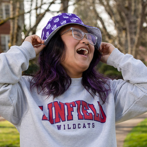 Female student wearing ѨƵ hoodie and hat, laughing.